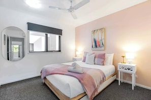 Ein Schlafzimmer mit einem Bett, einem Deckenventilator, einem Fenster, einem Gemälde und einem Nachttisch mit einer Lampe.