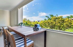 Ein Balkon mit Holztisch, Stühlen und Blick auf Grünflächen und Gebäude.