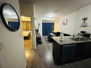 Compact apartment with a kitchenette and living area, featuring a small island with a sink and microwave, and a comfortable sofa.