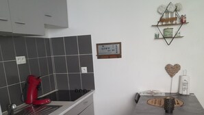 A compact kitchen with grey cabinets, a red kettle, and a small stool.
