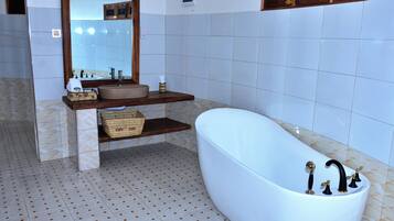 Ein Badezimmer mit freistehender Badewanne, einem Waschtisch mit Spiegel und einem Fliesenboden.
