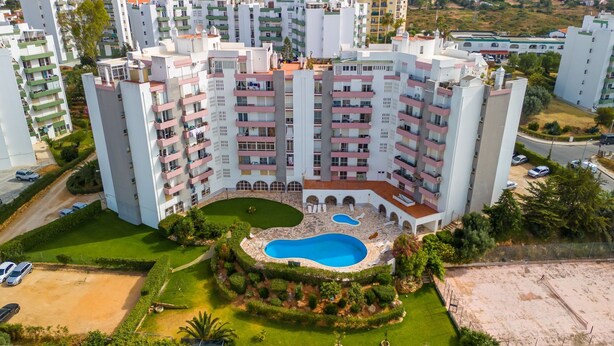 Un immeuble résidentiel de grande hauteur doté de nombreux balcons, d’une cour intérieure avec une piscine et d’un espace verdoyant environnant.