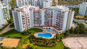 Un immeuble résidentiel de grande hauteur doté de nombreux balcons, d’une cour intérieure avec une piscine et d’un espace verdoyant environnant.