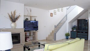 Una sala de estar con un sofá, una mesa de centro de cristal, una chimenea, un televisor y una escalera.