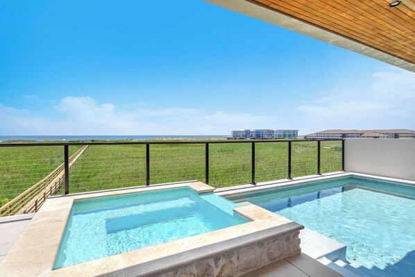 Ein Pool auf dem Dach mit klarem, blauem Wasser, umgeben von einem schwarzen Metallgeländer, mit Blick auf eine grüne Landschaft und ein entferntes Gebäude.