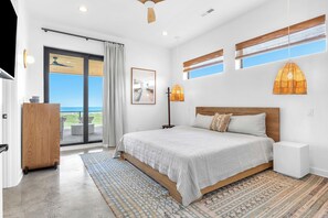 Ein Schlafzimmer mit einem großen Bett, Blick durch eine Schiebetür, Deckenventilator und Pendelleuchte.