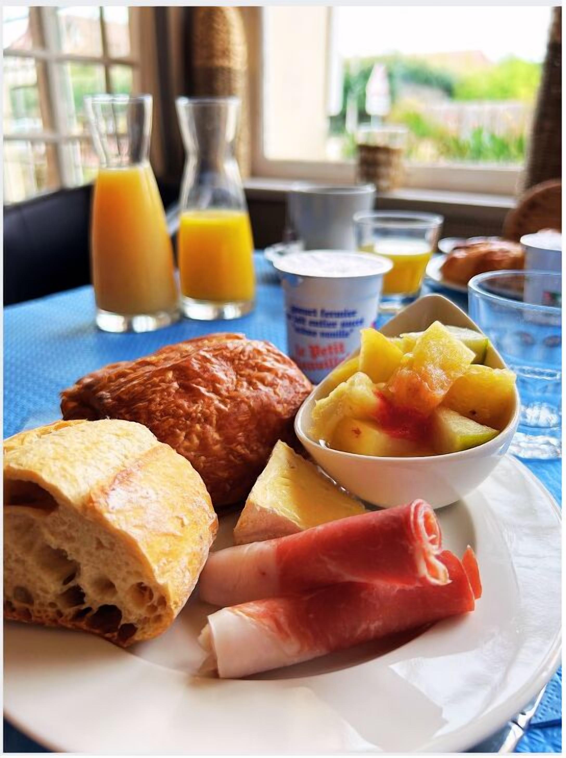 A breakfast plate with croissant, ham, and fruit salad, accompanied by orange juice and yogurt.
