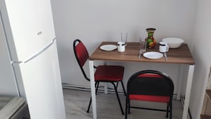Une cuisine de taille réduite, avec un réfrigérateur blanc, une cuisinière et deux chaises dotées de coussins rouges.