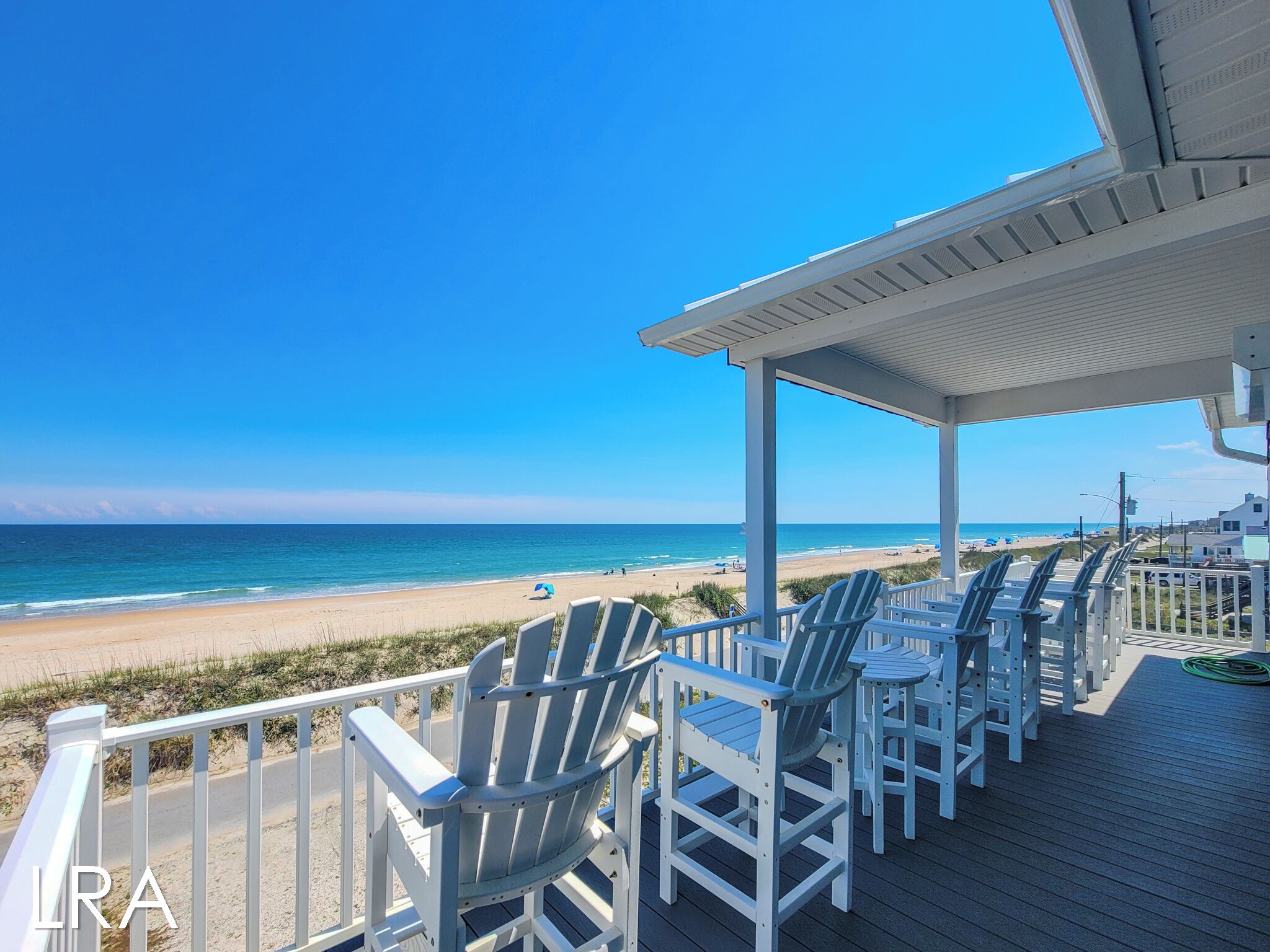 A covered deck with Adirondack chairs overlooking a beach.