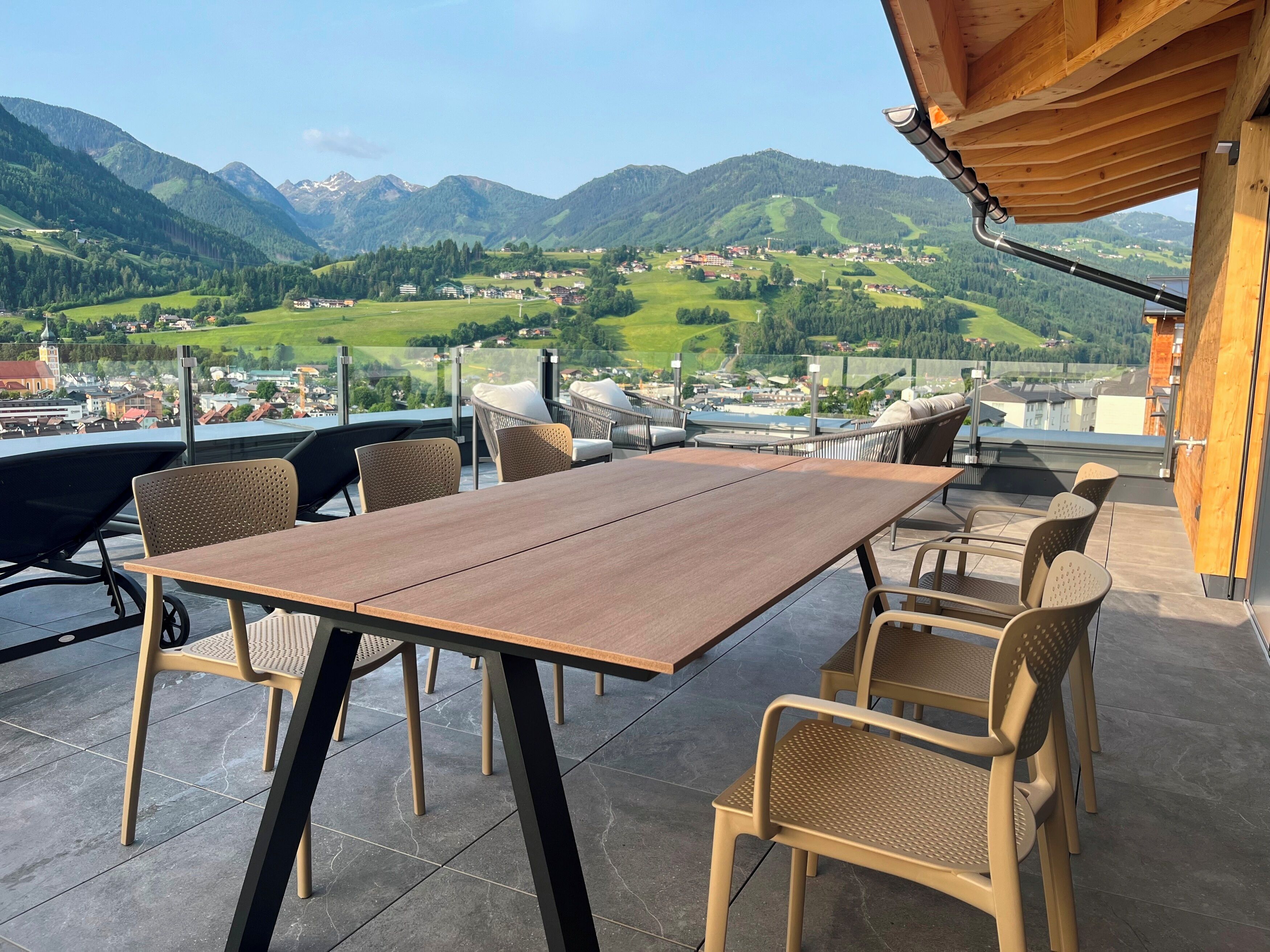 Una terraza con una mesa y sillas de madera, con vistas a un paisaje montañoso.