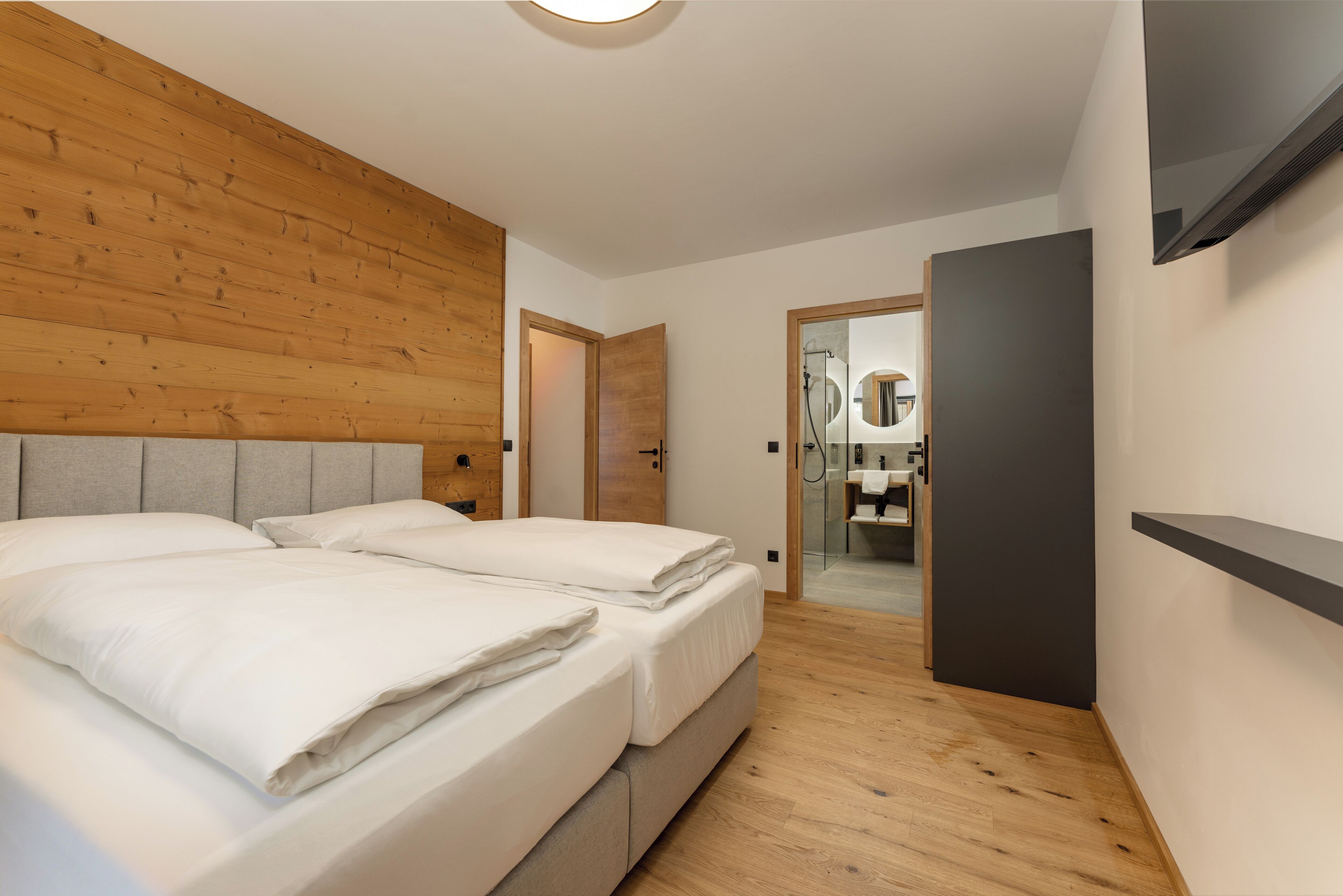 Ein Schlafzimmer mit zwei Betten, einem hölzernen Kopfteil und einem an der Wand montierten Fernseher.