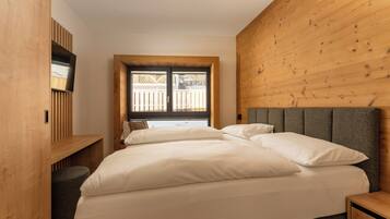 A bedroom with a bed, a wooden headboard, a TV mounted on a wooden panel, and a window with a view of a wooden deck.