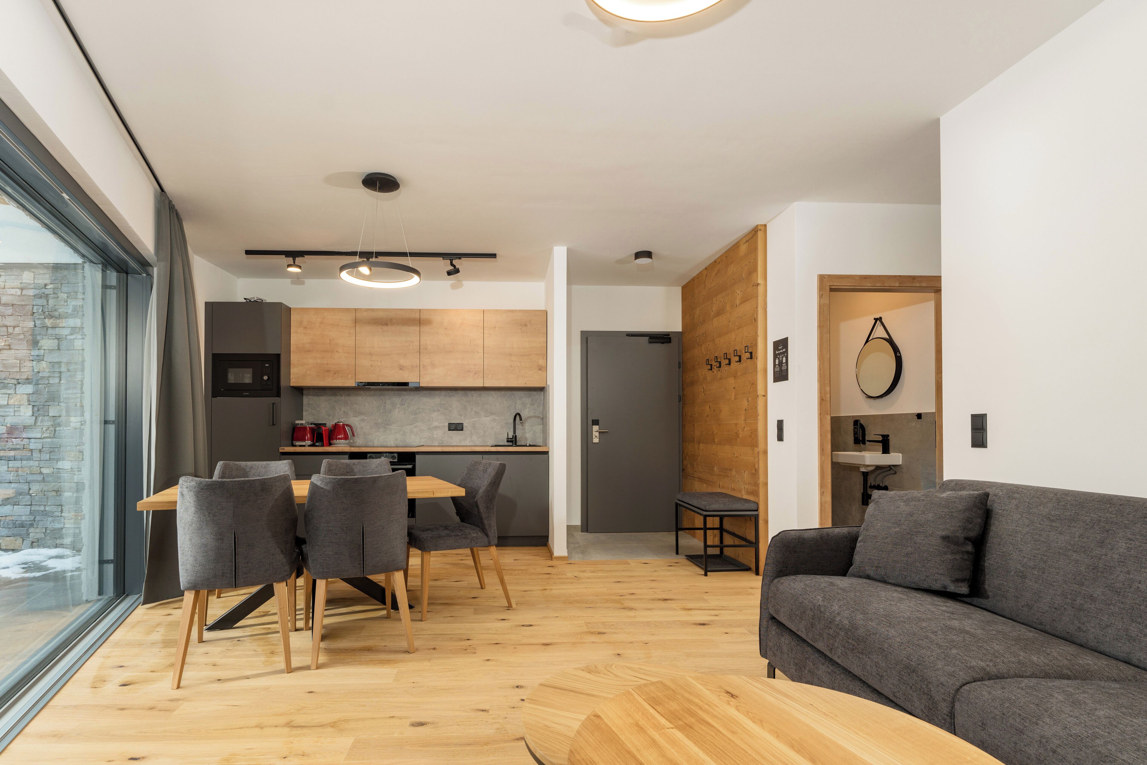 A modern living space with a dining area, a sofa, and a kitchen.