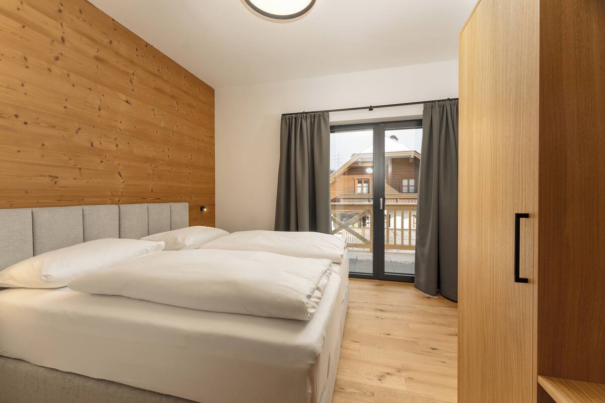 Une chambre à coucher avec un lit, une tête de lit en bois et une vue sur un balcon avec des rideaux.