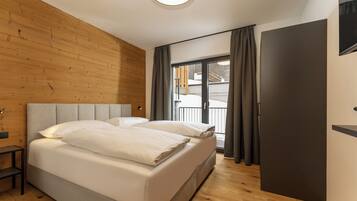 Un dormitorio moderno con cabecera de madera, una cama grande con ropa blanca, una mesita de noche pequeña y vistas a un balcón a través de una puerta corredera.