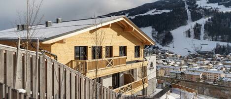 Una cabaña de madera con balcón, con una imponente montaña nevada de fondo.