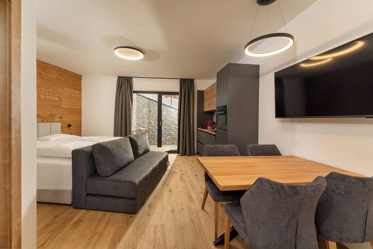 Une pièce moderne avec un plancher en bois, un canapé gris, une table à manger en bois et des chaises grises.
