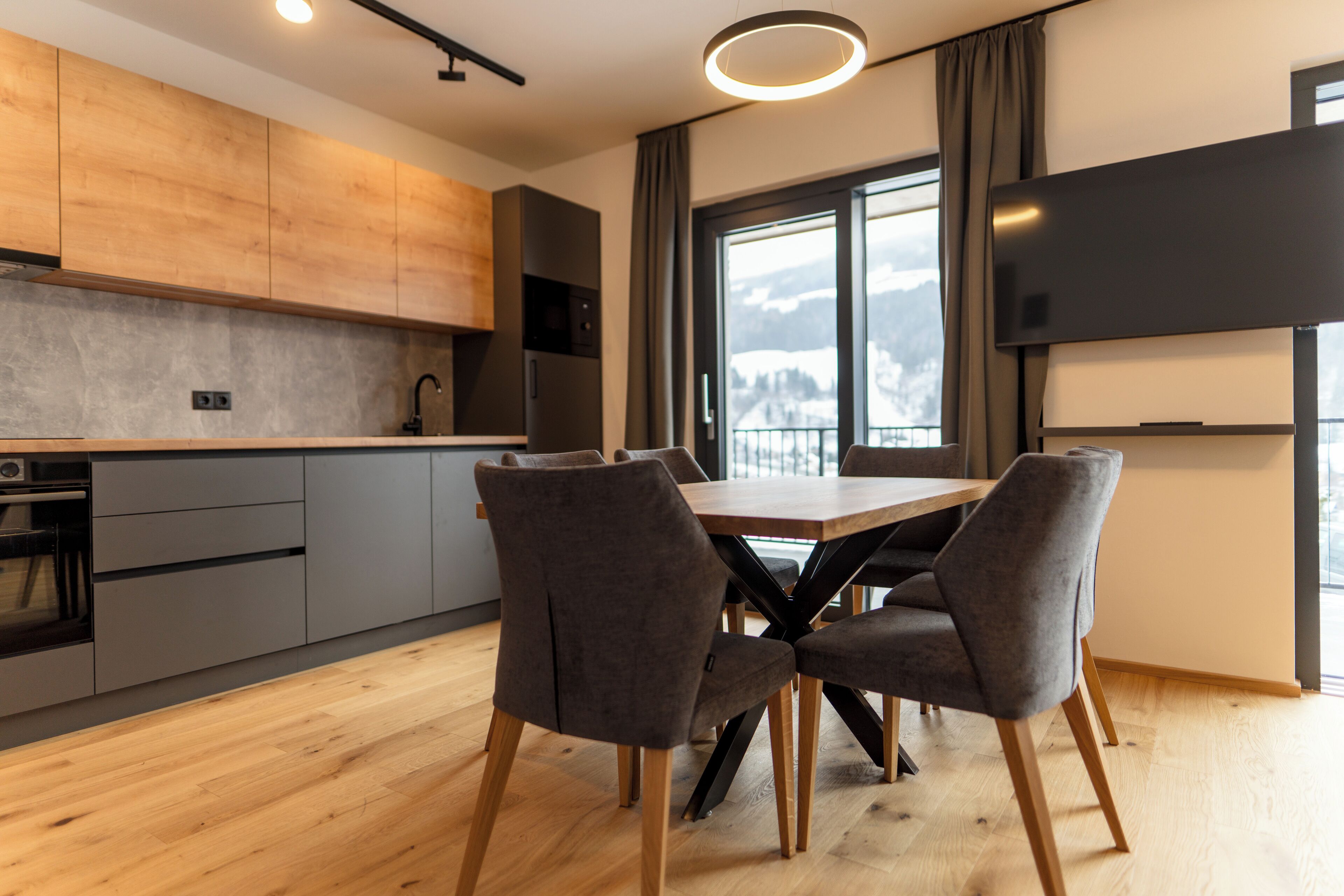 A modern kitchen with grey cabinets, a wooden countertop, and a dining area with a table and chairs.