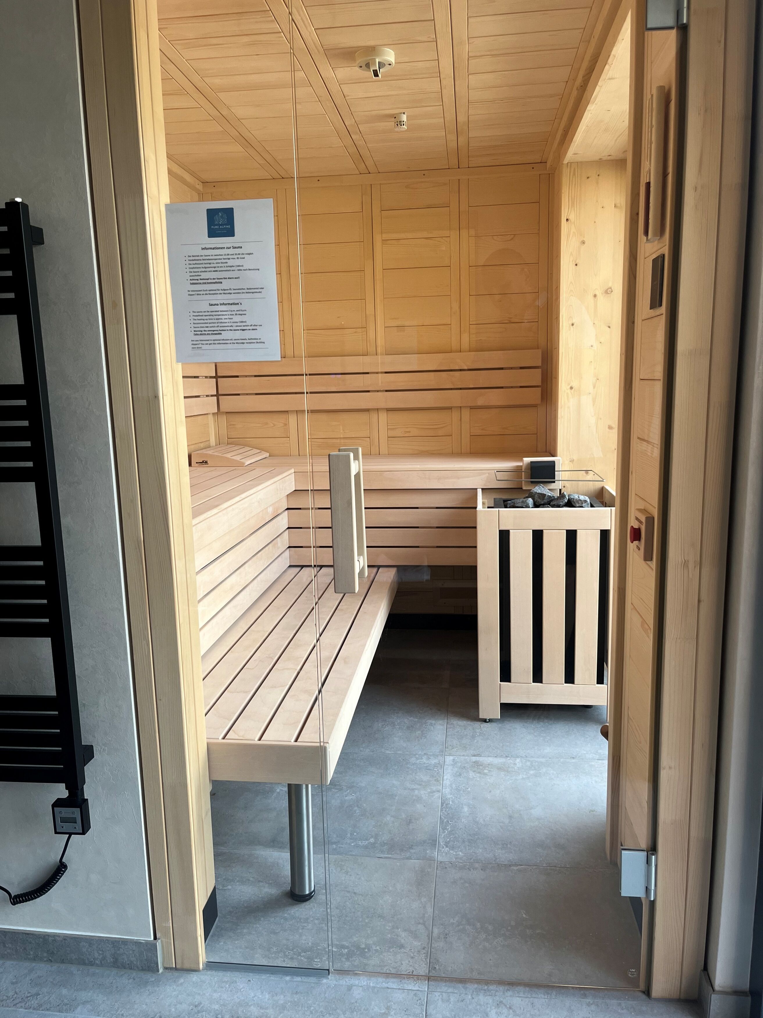 Un sauna avec des bancs en bois, une petite table avec un radiateur et un panneau d’information sur le sauna.
