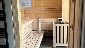 Ein Saunaraum mit Holzbänken, einem Tisch mit Heizung und einem Schild mit Informationen zur Sauna.