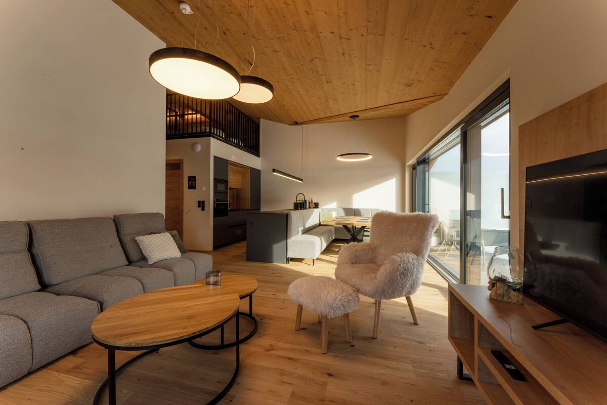 Un salon moderne avec un canapé, un fauteuil moelleux, une table basse en bois et un téléviseur.