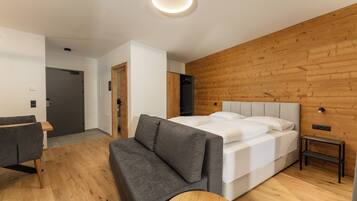 Un dormitorio moderno con una cama grande, un sofá gris, una mesita pequeña y paneles de madera en las paredes.