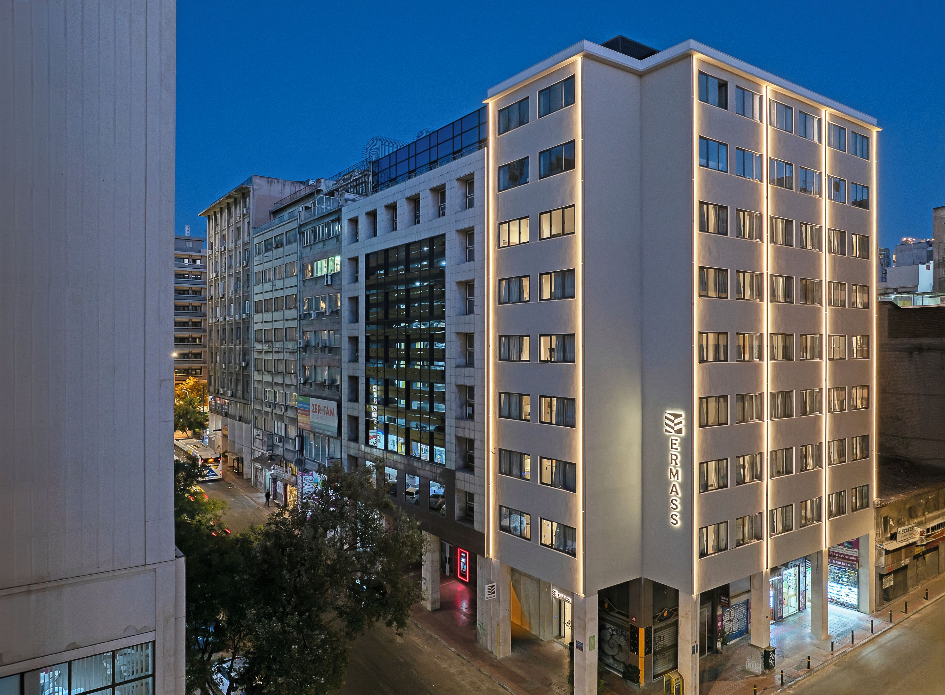 Un hôtel moderne à plusieurs étages, doté de grandes fenêtres et d’une enseigne « ERMASS » bien visible.