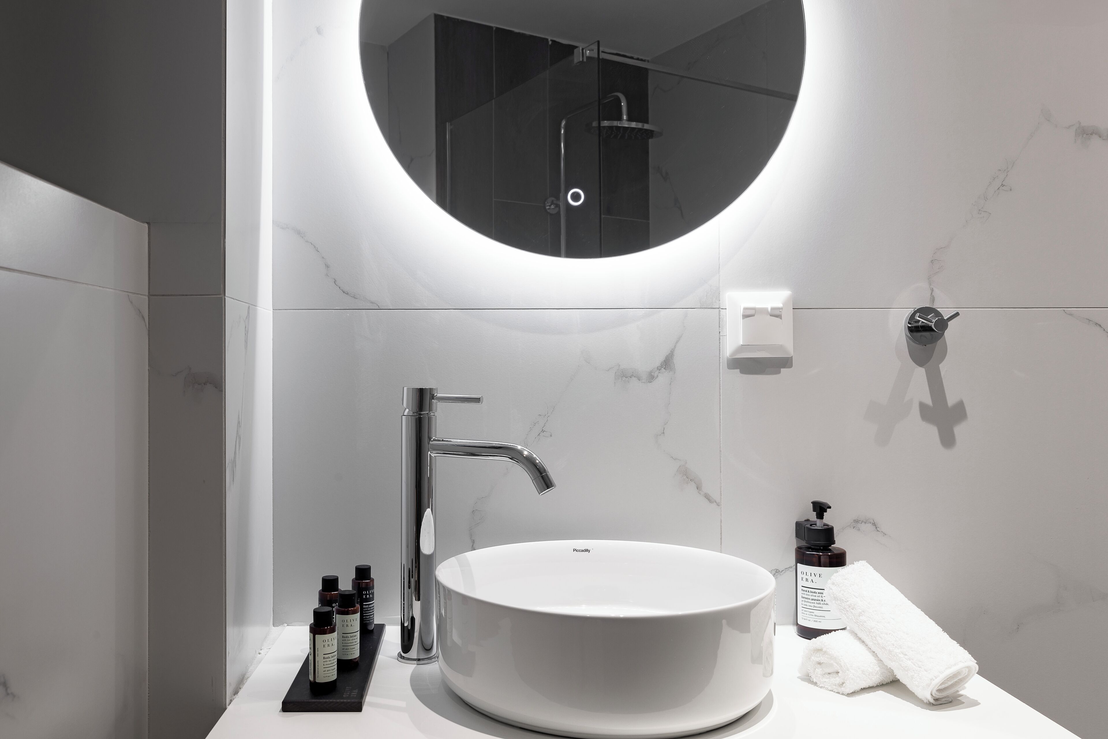 A modern bathroom with a round mirror, a white sink, and a handheld showerhead.