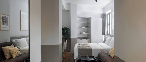 Una habitación de hotel moderna con una cama, un sofá, una mesita y una estantería.