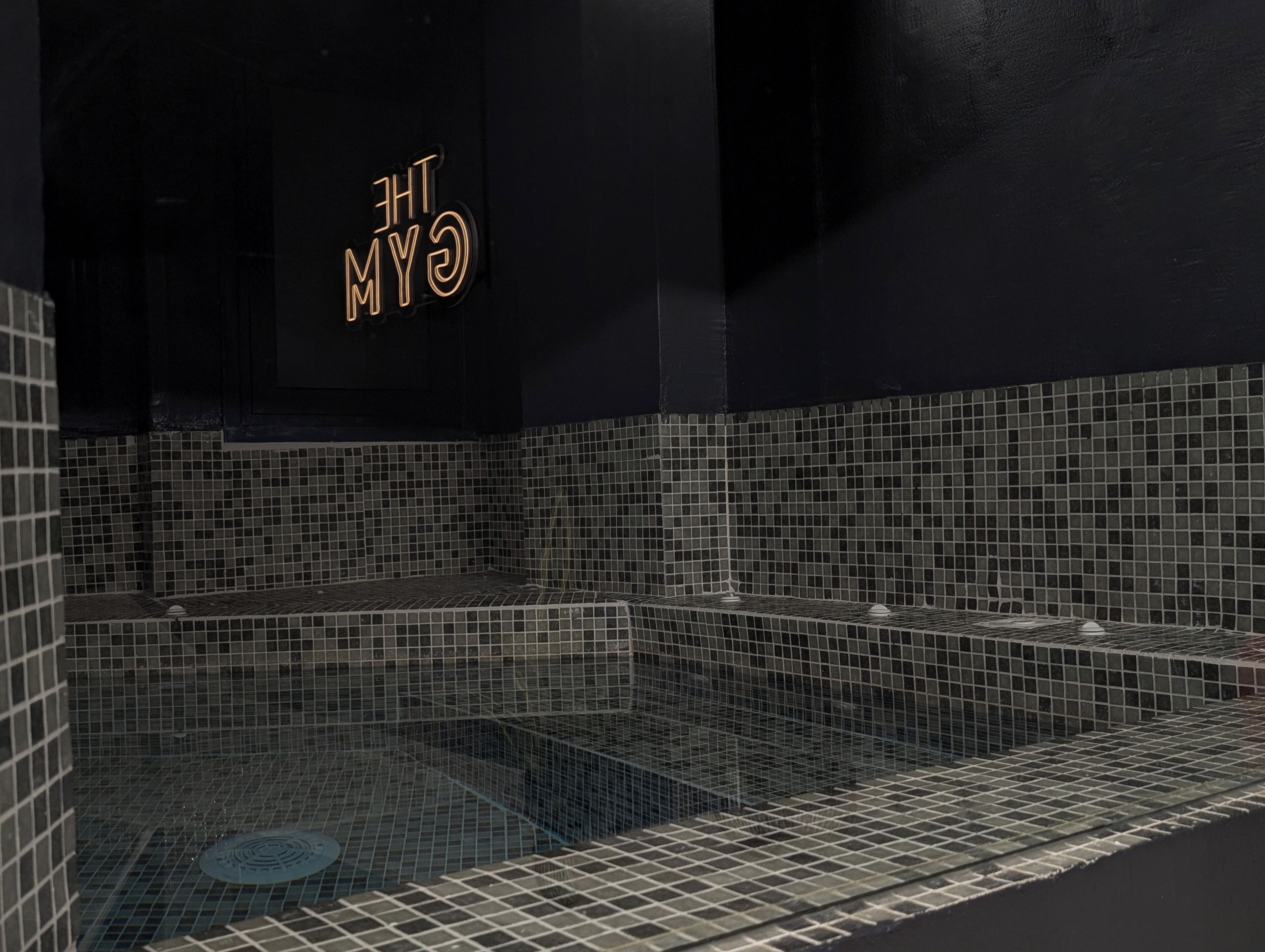 Un baño con baldosas, una pared negra y un cartel que dice 'THE GYM'.