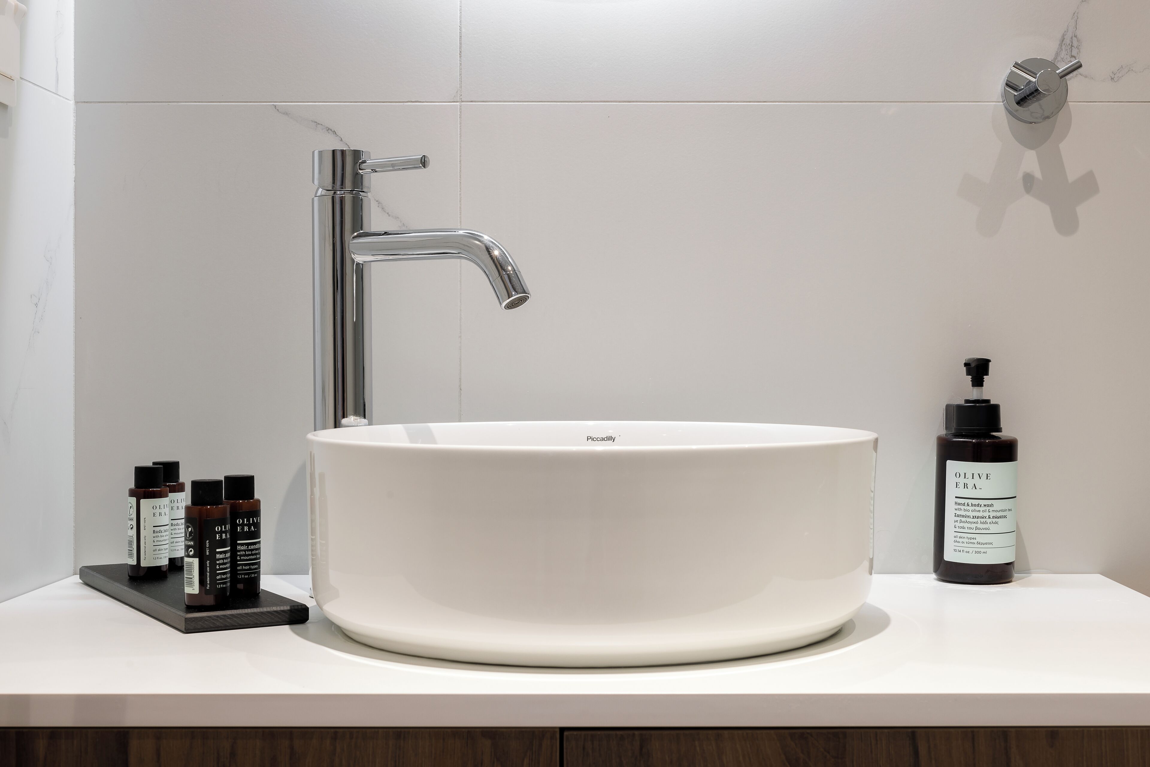 A modern bathroom with a white sink, chrome faucet, and a bottle of olive oil.