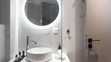 Un baño moderno con un espejo redondo, un lavabo blanco y un mueble de tocador de madera.