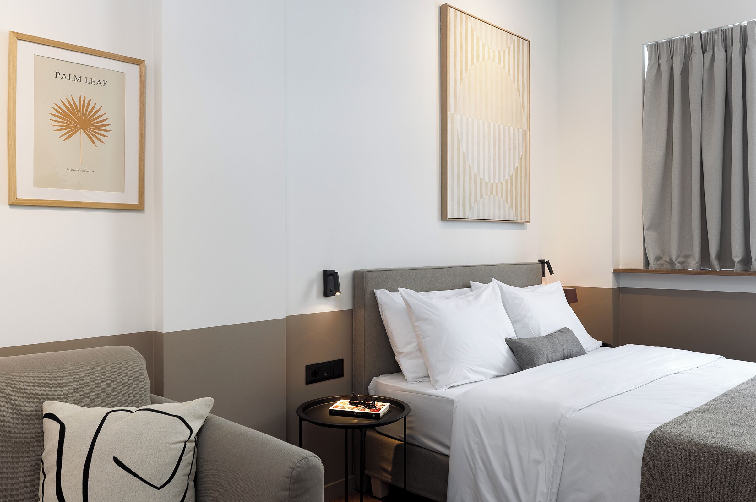 A hotel room with a bed, a nightstand, a framed artwork, and a window with curtains.