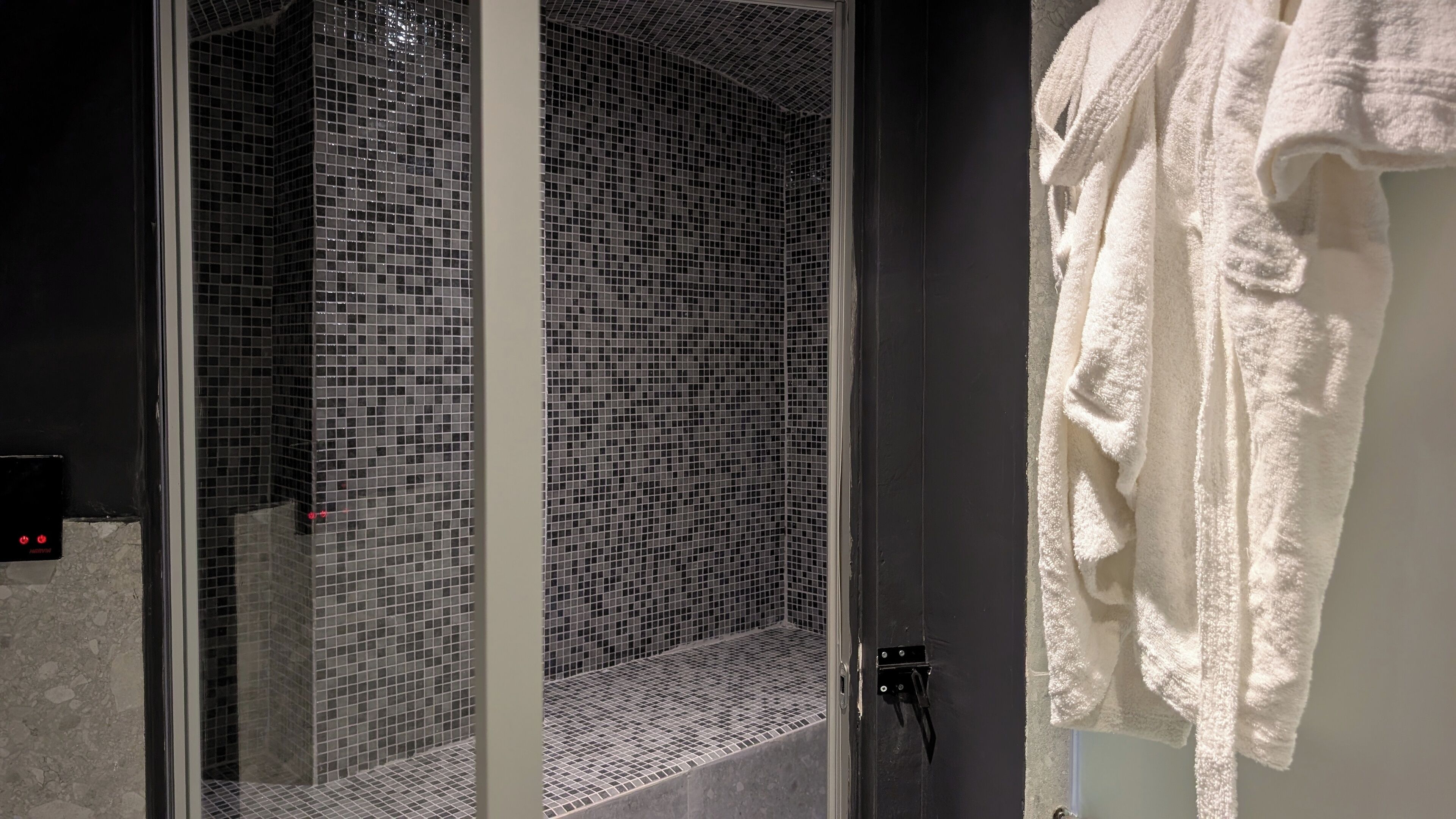 Un baño con cabina de ducha de vidrio, una toalla blanca colgada en la pared y un panel de control en la pared.