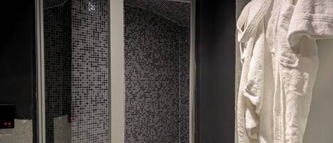 Une salle de bain avec une douche à parois de verre, une serviette blanche accrochée au mur et un panneau de commande fixé au mur.