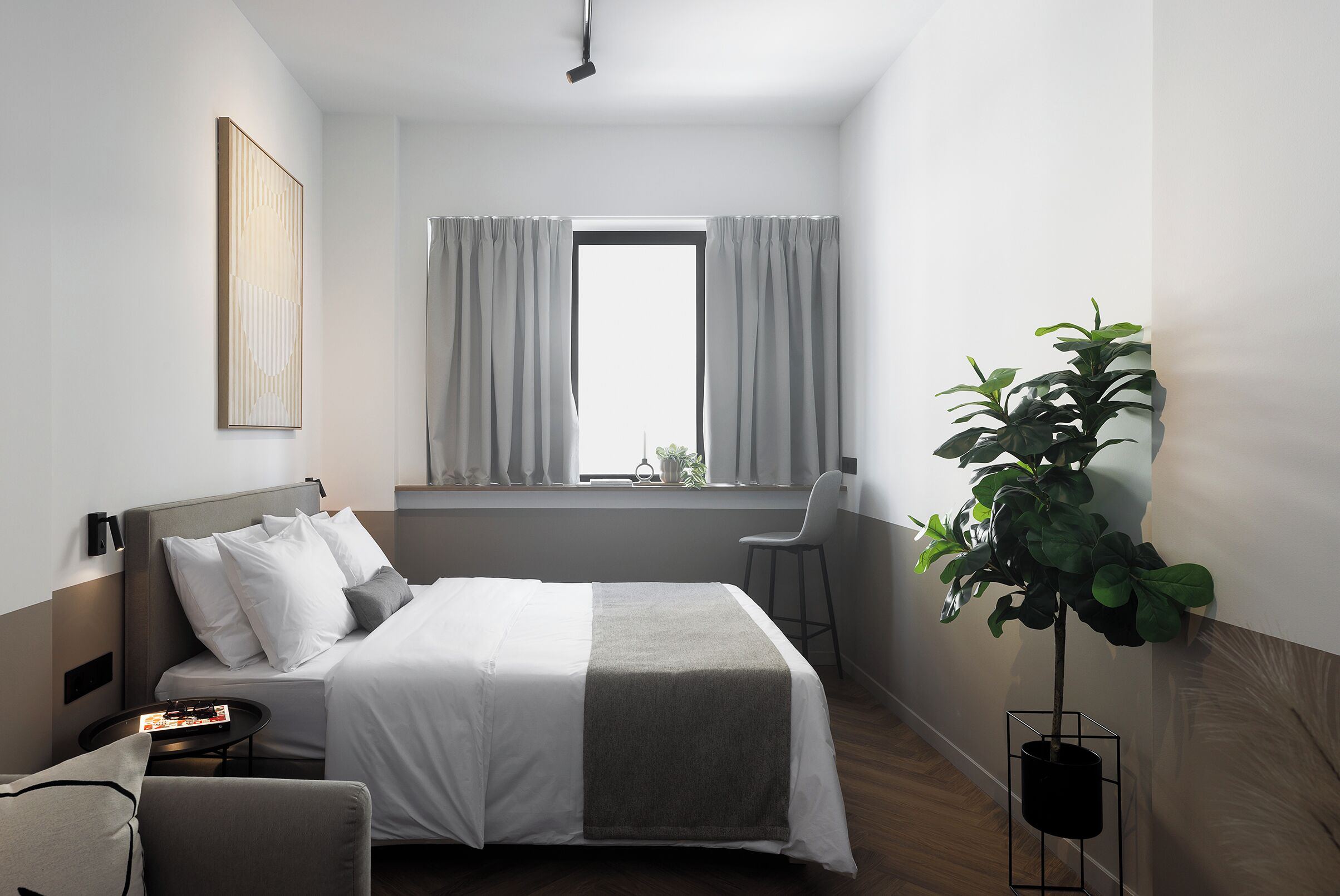 A modern hotel room with a bed, a chair, a small table, and a potted plant.