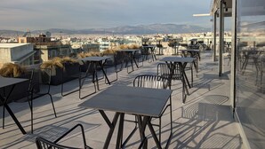 A rooftop terrace with tables and chairs, offering a view of a cityscape and mountains. - ERMASS Athens (Athens)