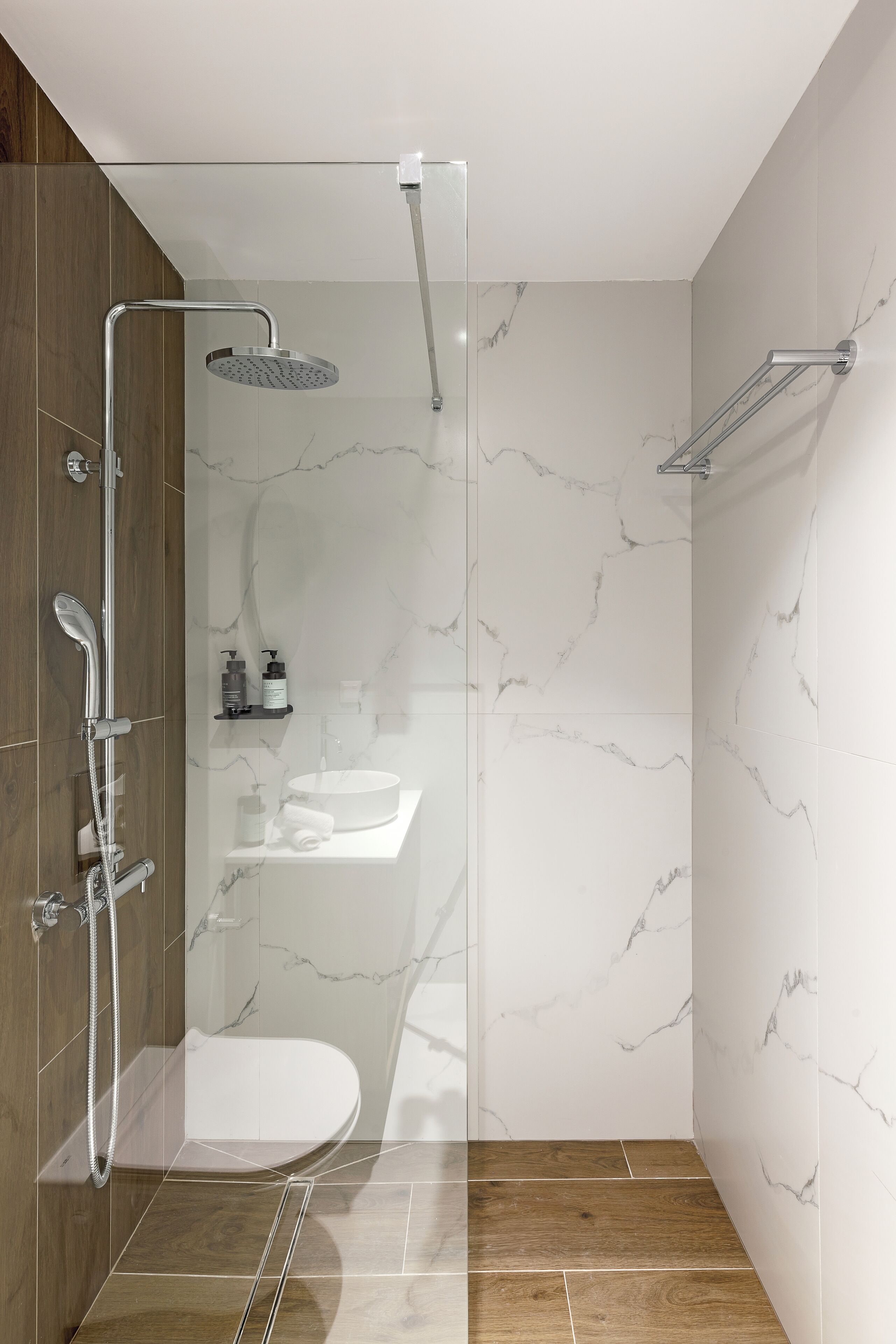 Een moderne badkamer met een douchecabine van glas, een witte wastafel en een houten opbergmeubel.