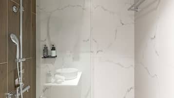 Een moderne badkamer met een douchecabine van glas, een witte wastafel en een houten opbergmeubel.