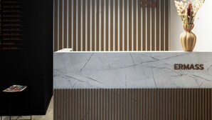 A reception desk with a marble top, vertical wooden slats, and a modern light fixture. - ERMASS Athens (Athens)