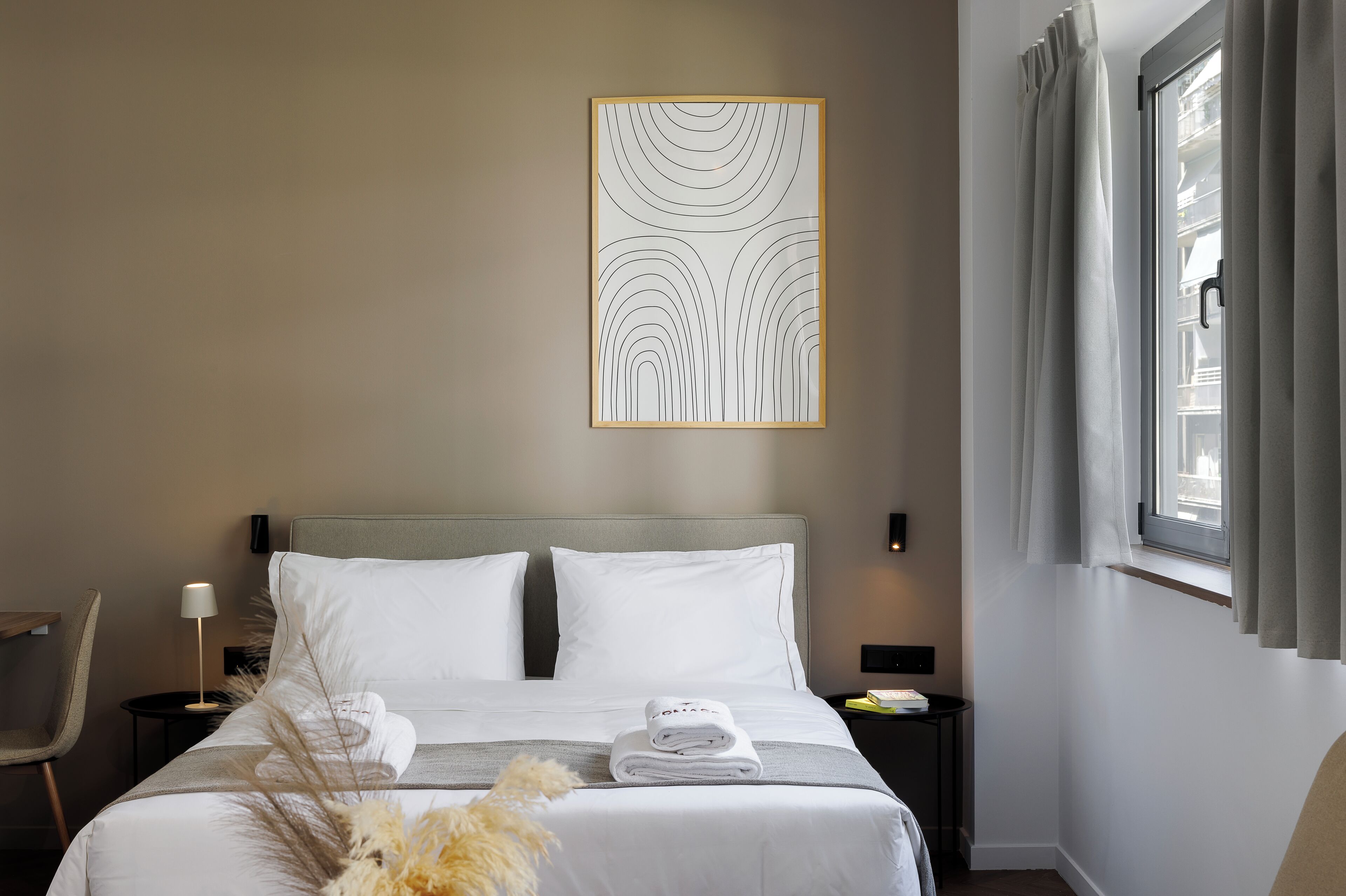 A neatly made bed with white linens, a bedside table with a lamp, and a wall-mounted artwork.