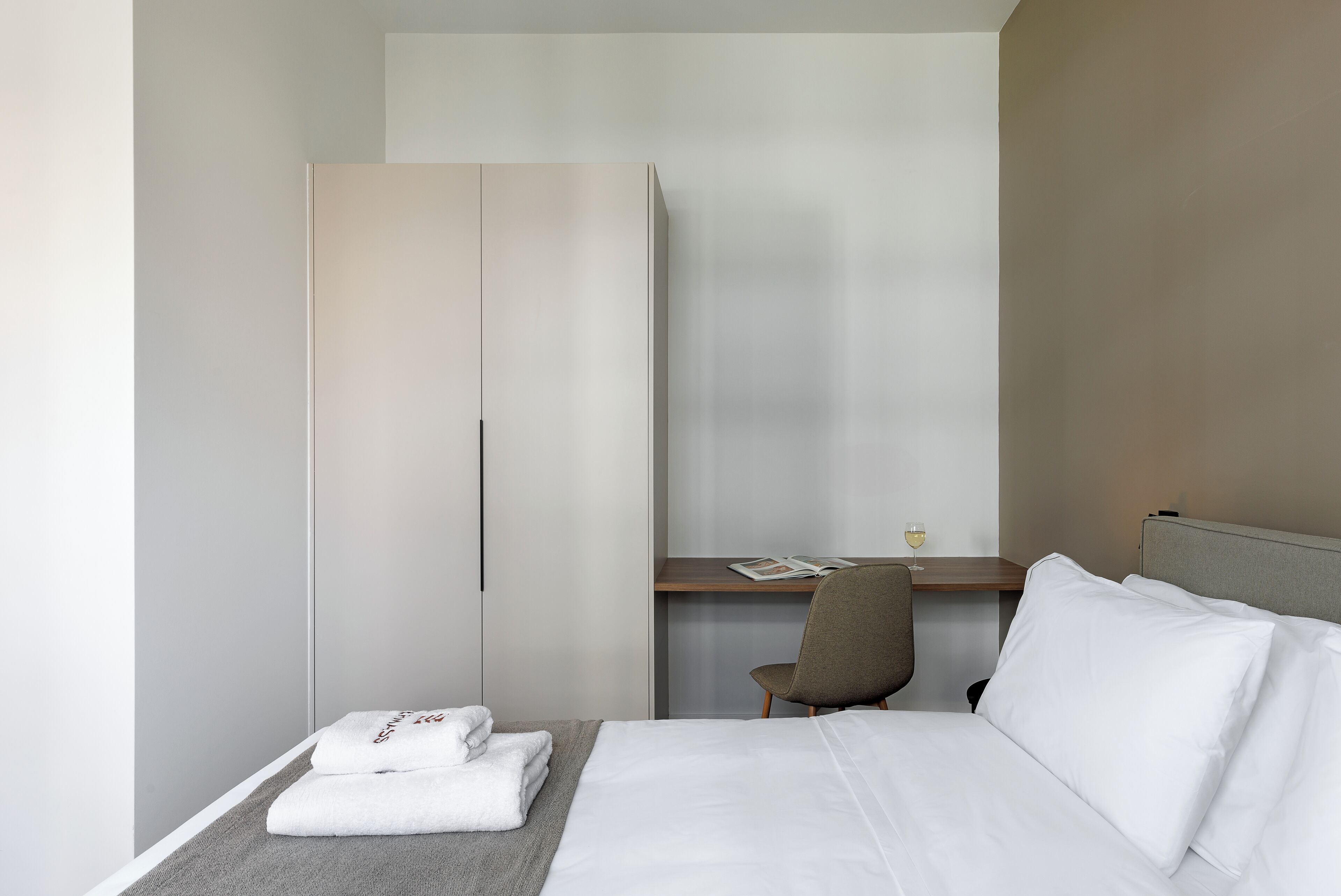 A hotel room with a bed, a desk, a chair, and a wardrobe.