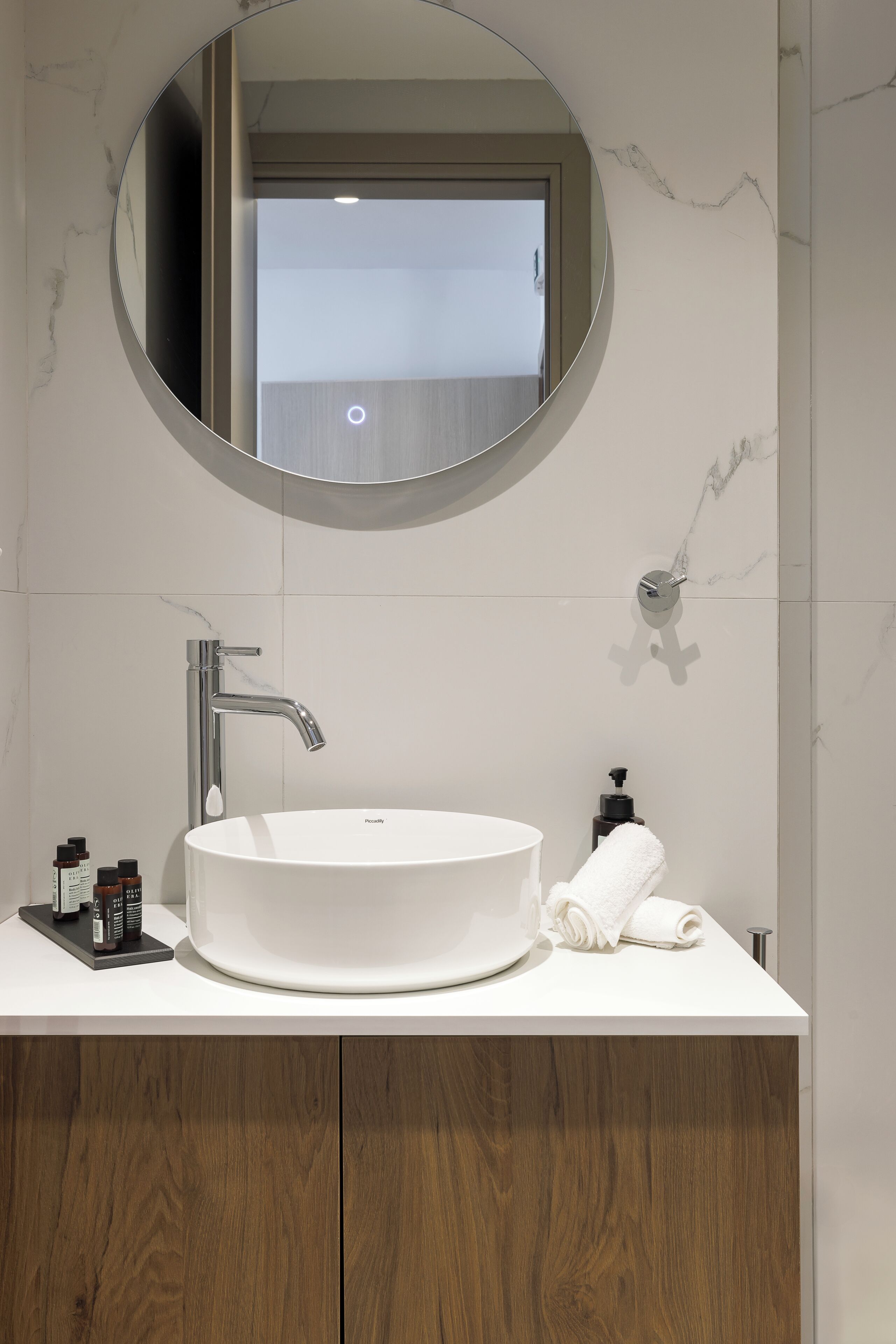 A modern bathroom with a round mirror, a white sink, and a wooden cabinet.