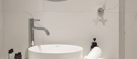 Un baño moderno con un espejo redondo, un lavabo blanco y un mueble de madera.