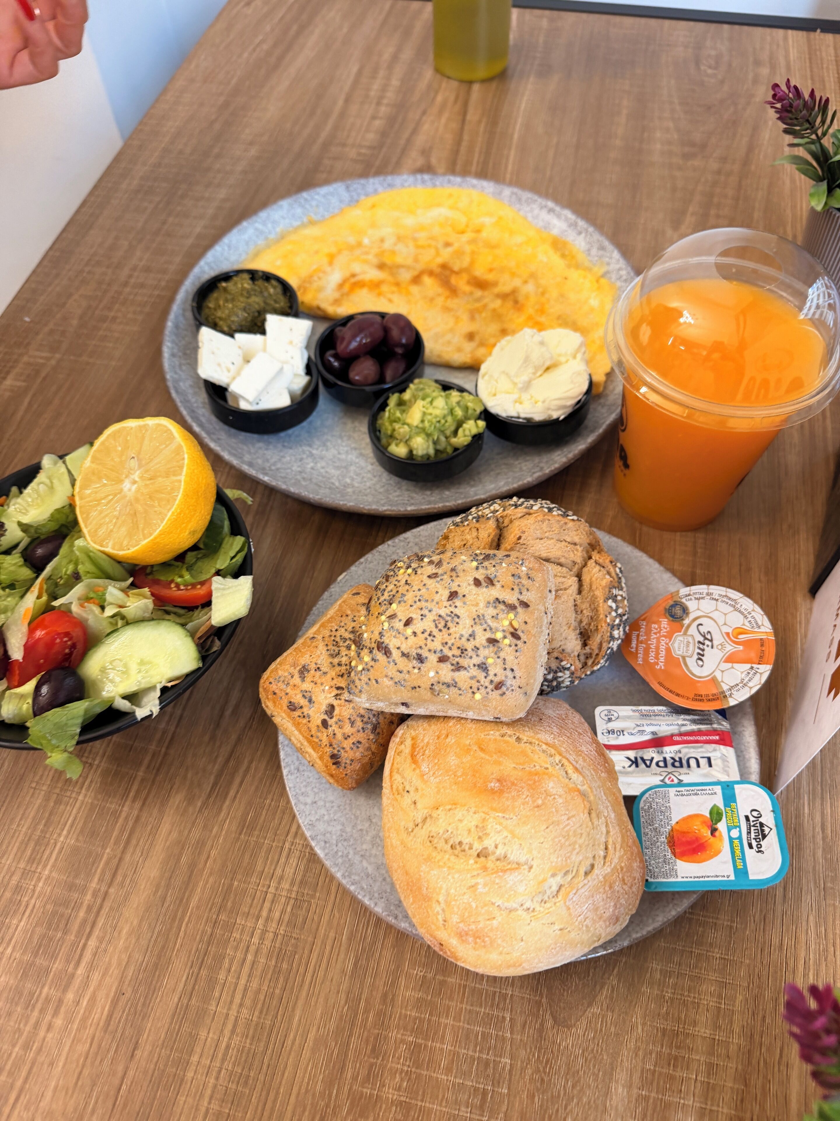 Eine Mahlzeit mit Brot, Käse, Oliven und einem Getränk auf einem Holztisch.