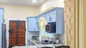 A compact kitchen with a dining area, featuring a refrigerator, microwave, and a small dining table with chairs. - Unit 1 - Downstairs Front (Georgetown)
