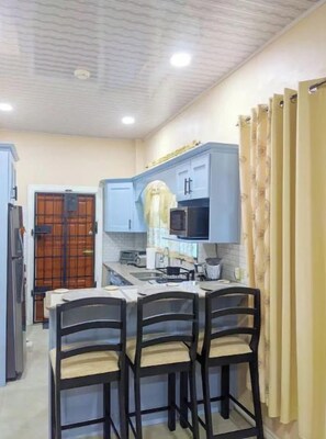 A compact kitchen with a dining area, featuring a microwave, cabinets, and a small island with chairs. - Unit 2 - Downstairs Back (Georgetown)