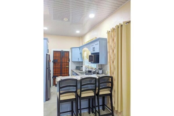 A compact kitchen with a dining area, featuring a microwave, cabinets, and a small island with chairs.