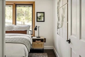 A bedroom with a bed, bedside table, lamp, and a window with a view of trees.