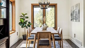 Ein Esszimmer mit großem Tisch, Stühlen, einer Chandelier, einem Blumentopf und einem Fenster mit Blick.